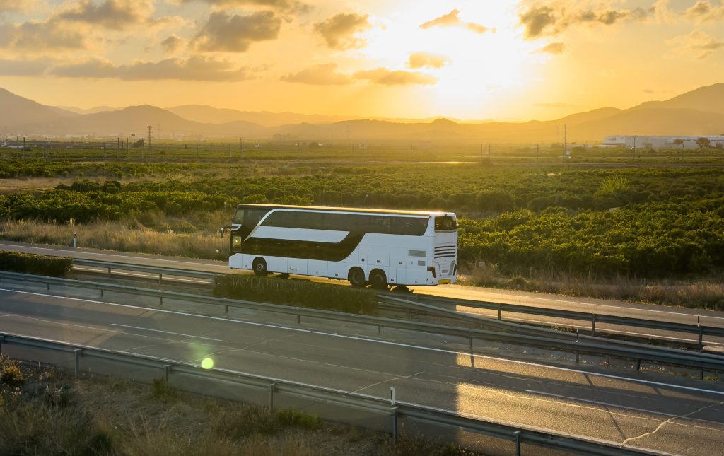 Autocar de tourisme sur une route au coucher du soleil, symbole des longues liaisons vers l'international
