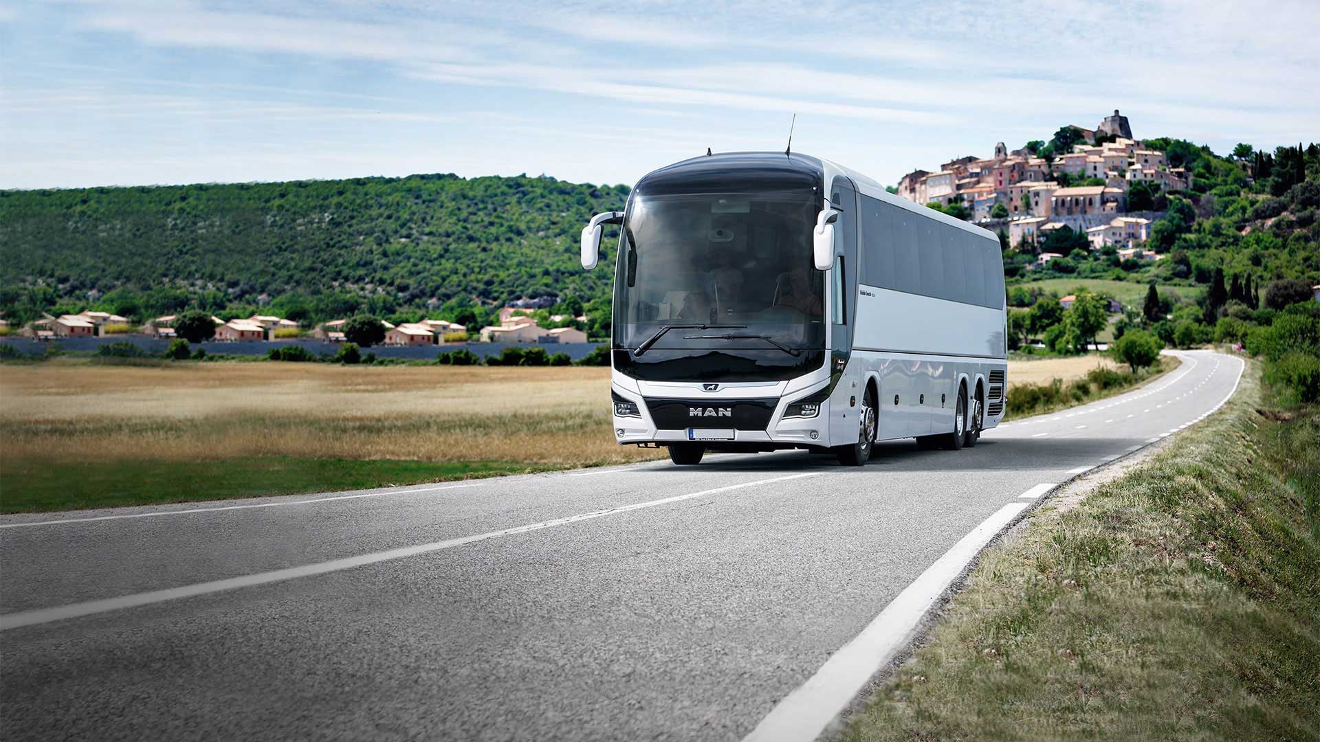 Autocar de tourisme blanc et noir circulant sur une route de campagne, illustrant les tarifs de location d'un bus avec chauffeur selon la distance