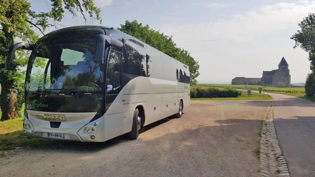 Autocar de tourisme stationné en bordure de route de campagne près d'une église, illustrant un trajet aller-retour en autocar avec chauffeur