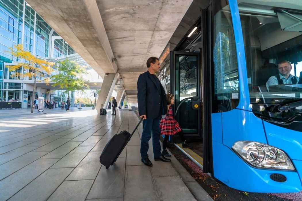 Père et sa fille embarquant avec leur valise à bord d'un bus bleu lors d'un transfert en bus vers l'aéroport