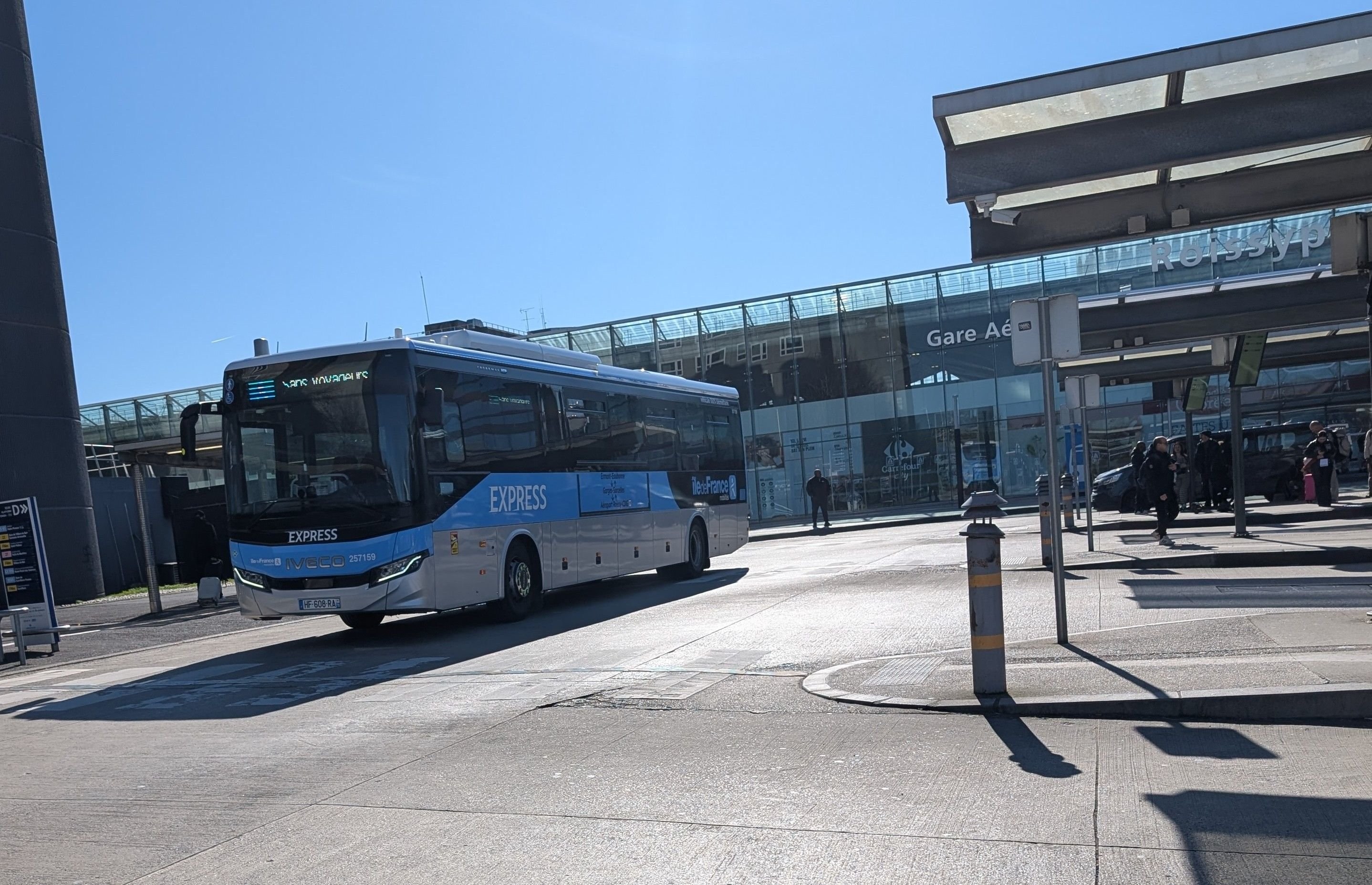 Bus express de transfert stationné devant la gare aéroportuaire de l'aéroport Charles-de-Gaulle sous un ciel bleu